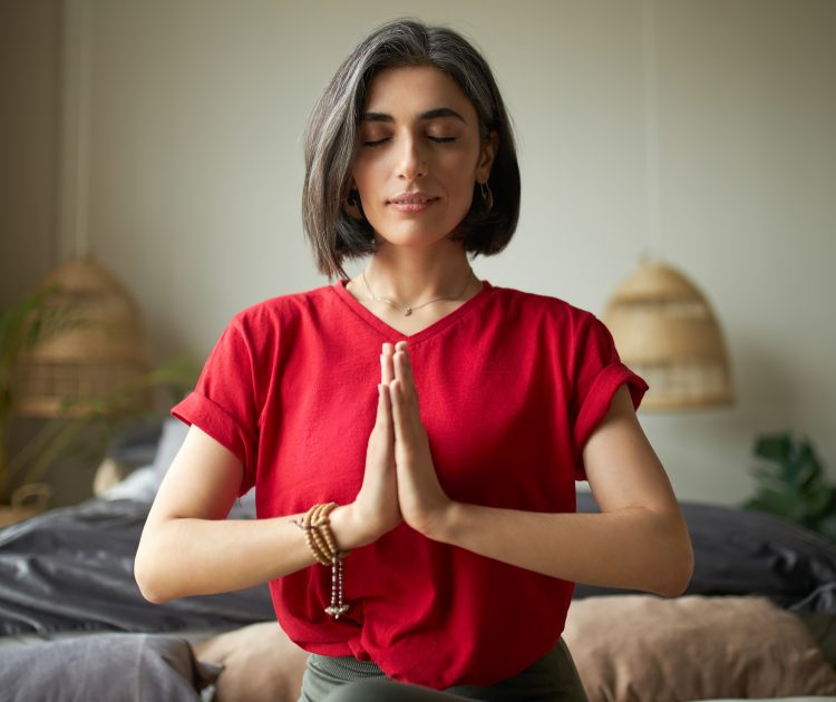 Self awareness and mindfulness concept. Attractive young woman having premature graying meditating at home with eyes closed, focusing on breathing, feeling present moment, making namaste gesture