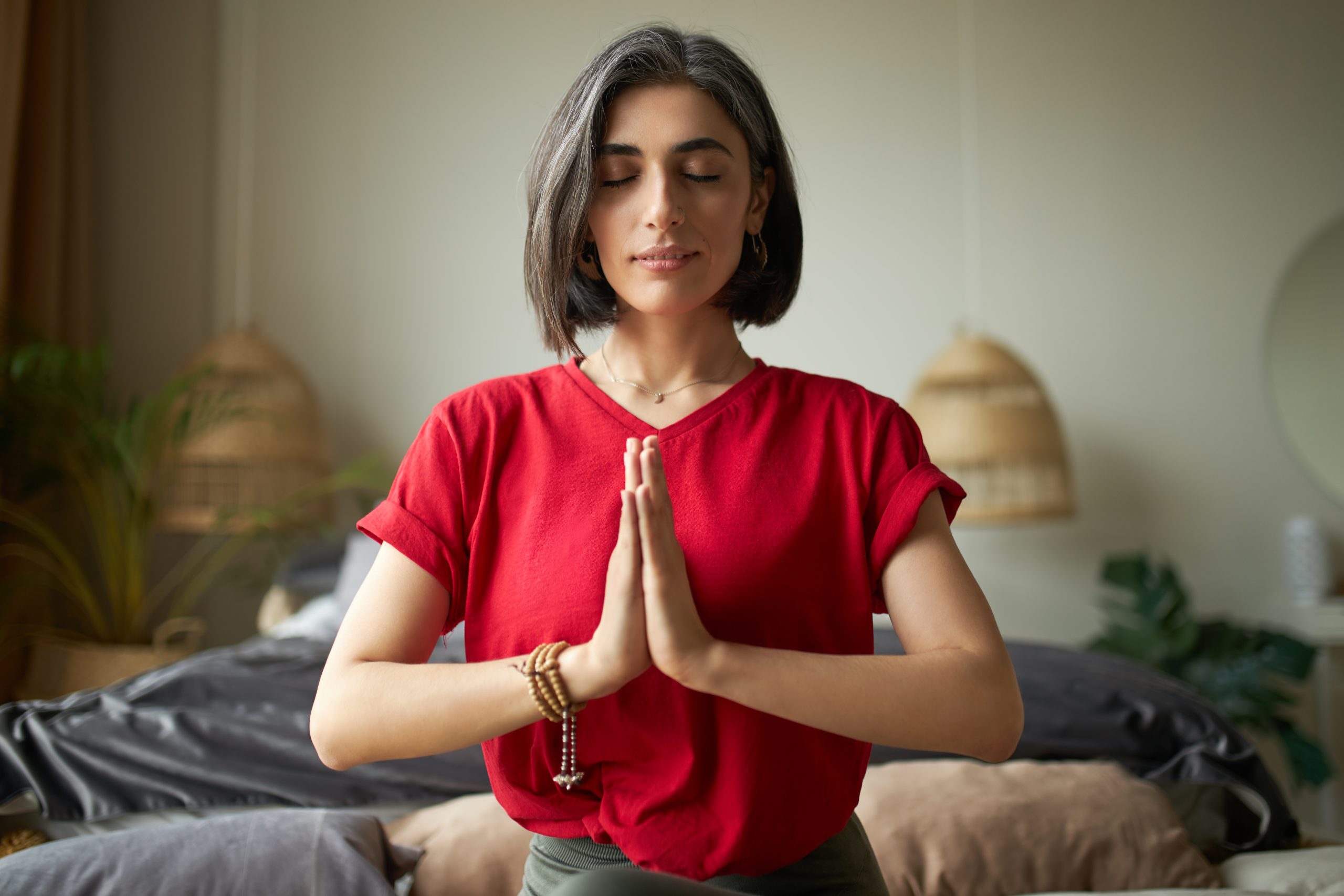 Self awareness and mindfulness concept. Attractive young woman having premature graying meditating at home with eyes closed, focusing on breathing, feeling present moment, making namaste gesture